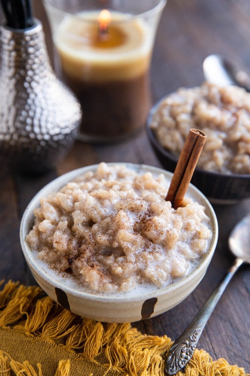 Two bowls of dairy-free rice pudding with a candle in the background and a spoon and golden napkin to the side.