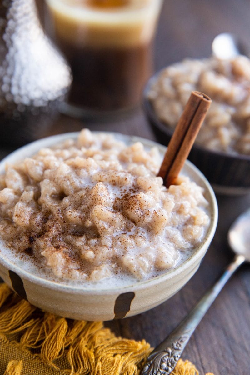 Two bowls of creamy rice pudding with a spoon to the side and cinnamon sticks in the rice pudding.