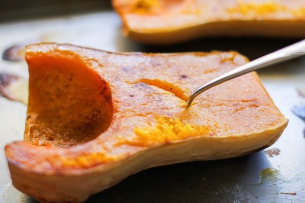 Roasted butternut squash fresh out of the oven with a spoon scooping at the flesh.