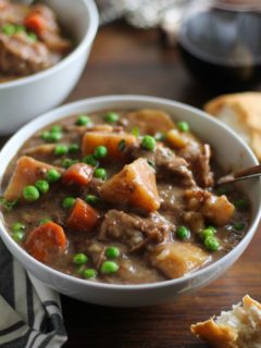 two white bowls of hearty beef stew on a rustic wood background with bread and wine to the side.