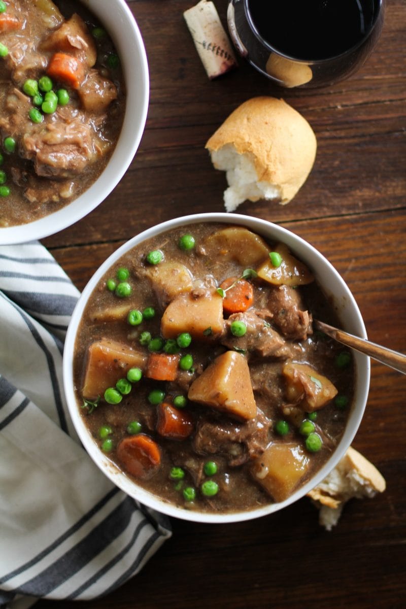 Top down photograph of white bowl of beef stew on a dark rustic wood background