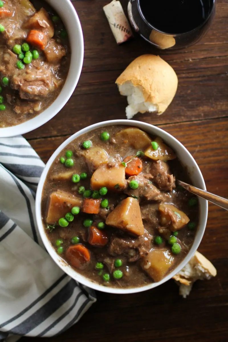 Top down photograph of white bowl of beef stew on a dark rustic wood background