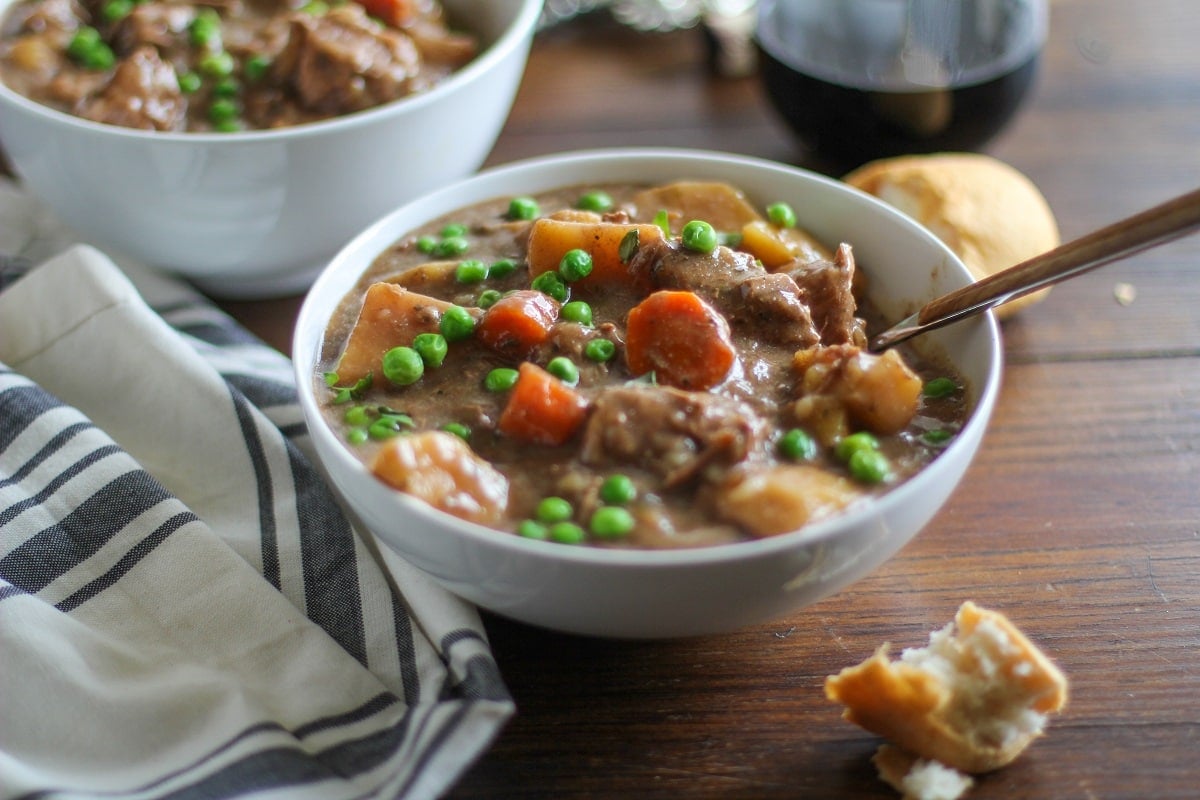 Horizontal image of a white bowl of beef stew on a wood background