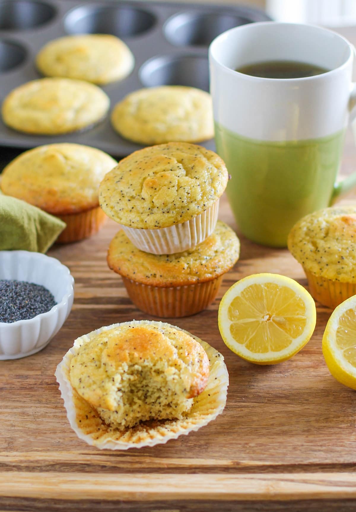 Grain-free lemon poppy seed muffins on a cutting board with a mug of tea in the background, ready to eat.