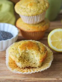 lemon poppy seed muffins on a wooden cutting board with a bite taken out of one of them.