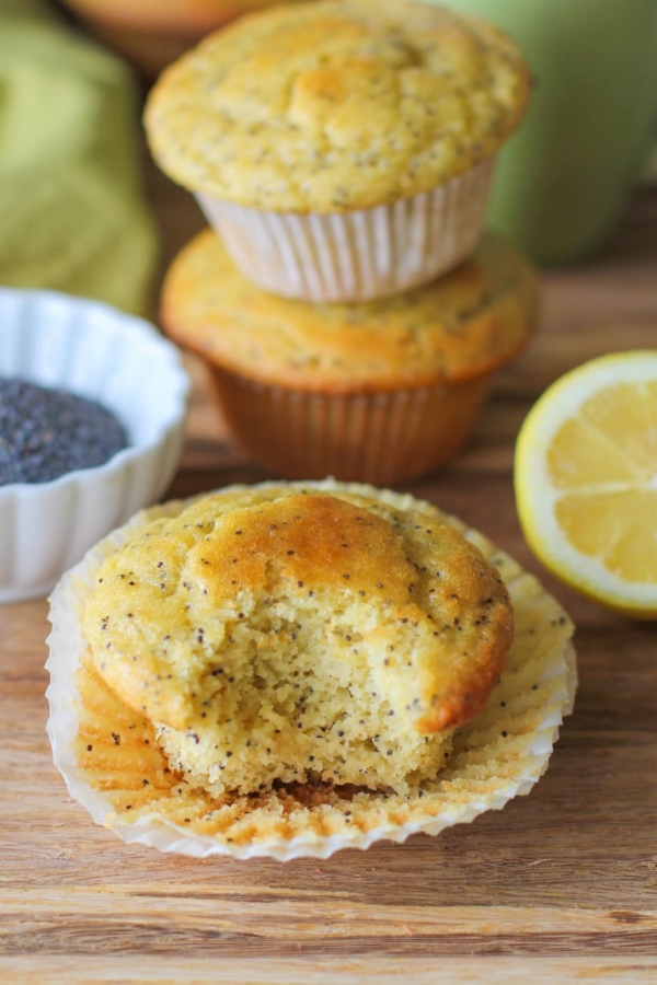 lemon poppy seed muffins on a wooden cutting board with a bite taken out of one of them.