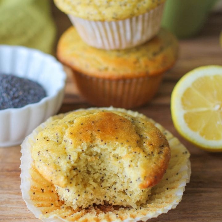 lemon poppy seed muffins on a wooden cutting board with a bite taken out of one of them.