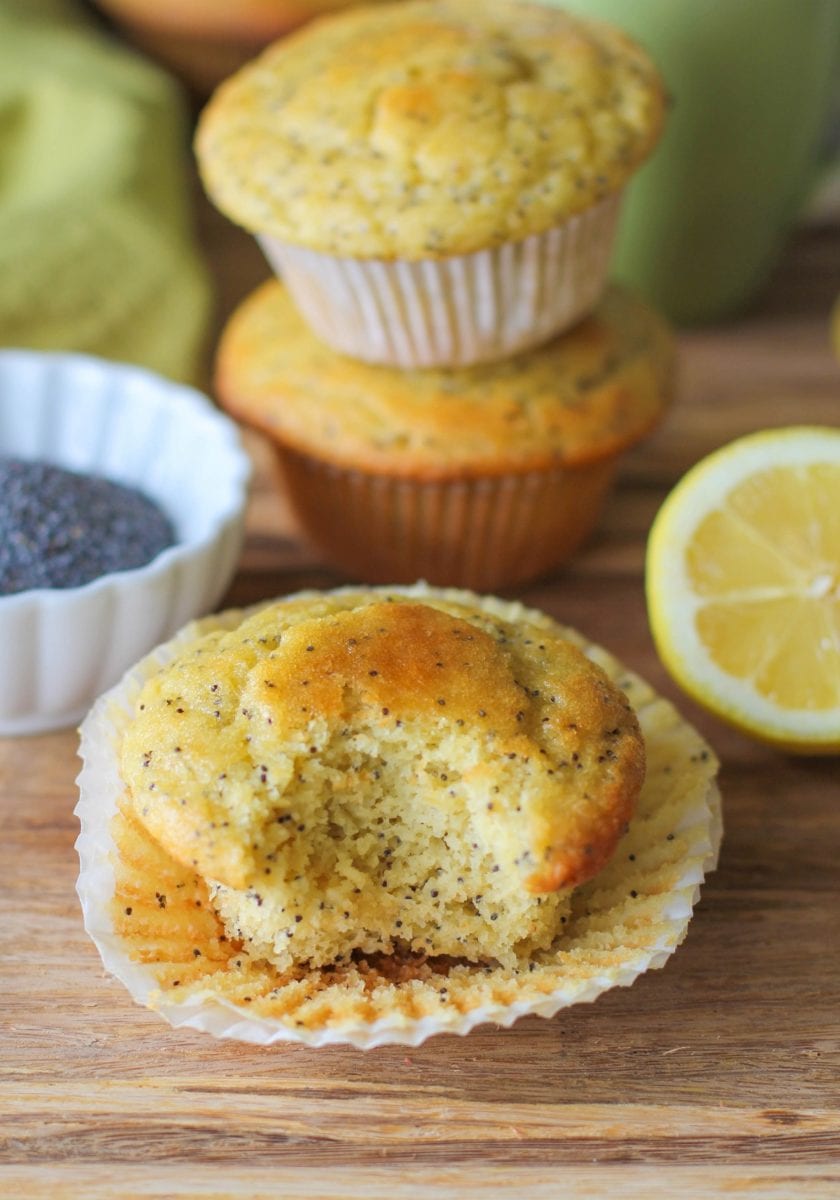 lemon poppy seed muffins on a wooden cutting board with a bite taken out of one of them.