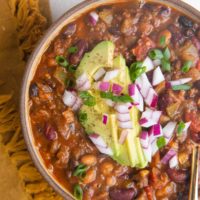 Top down bowl of turkey chili with sliced avocado, green onions and red onions on top