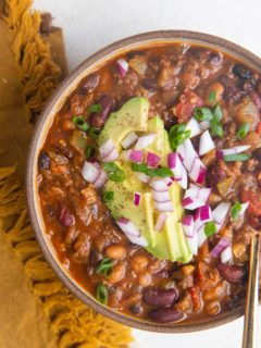 Top down bowl of turkey chili with sliced avocado, green onions and red onions on top