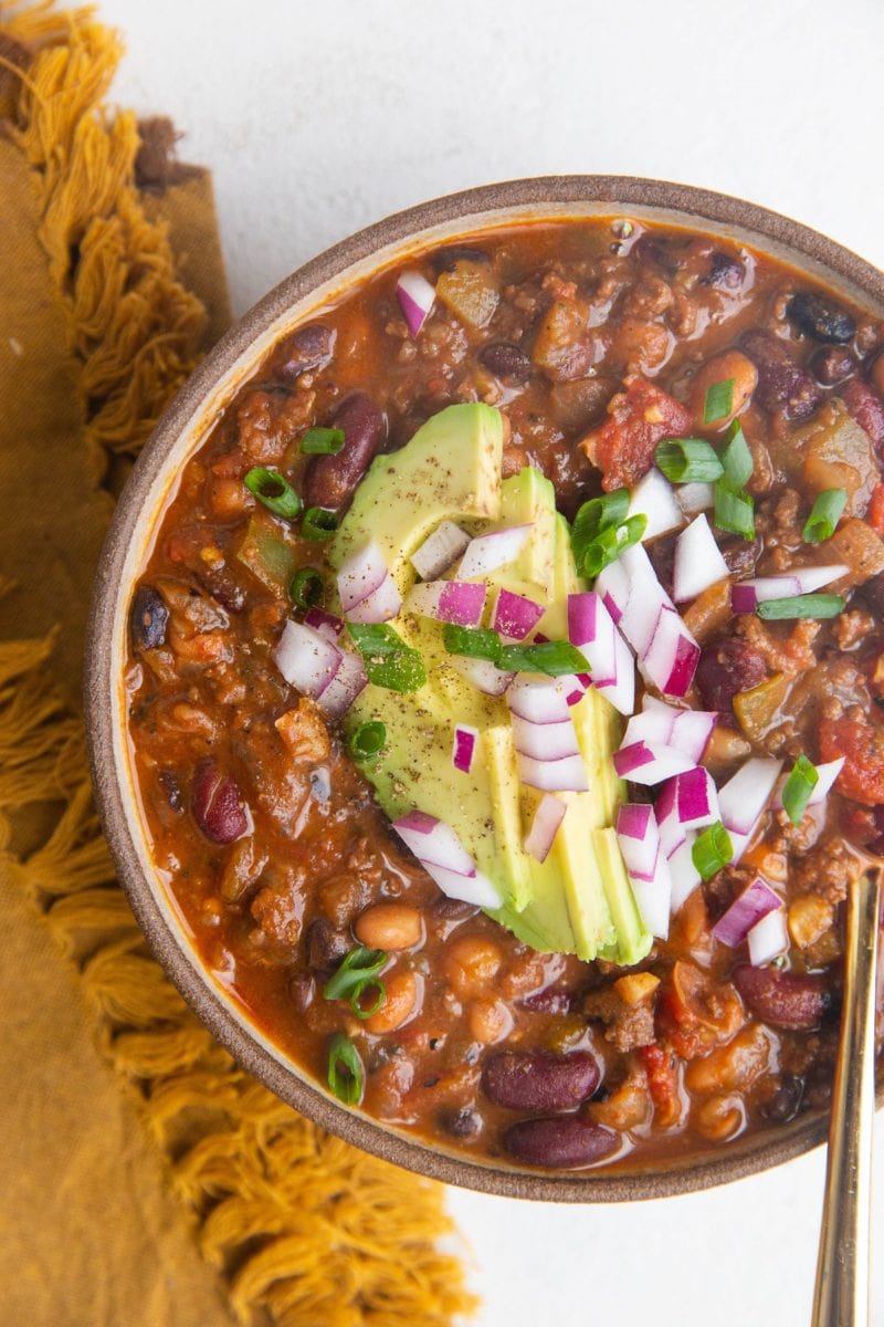 Top down bowl of turkey chili with sliced avocado, green onions and red onions on top