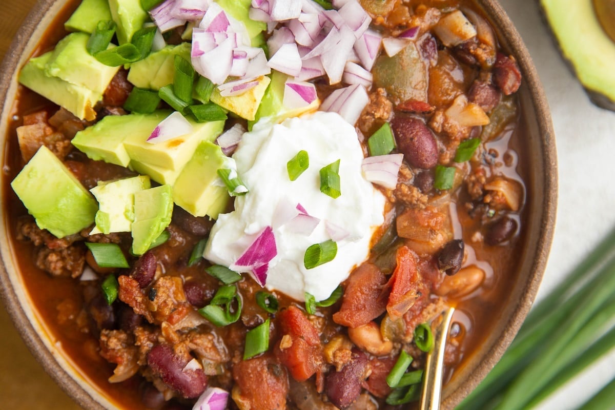 Horizontal photo of turkey chili in a big ceramic bowl with onions and sour cream on top.
