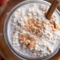 Top down close up image of a jar full of Chai spiced overnight oats with a cinnamon stick inside and a red napkin.