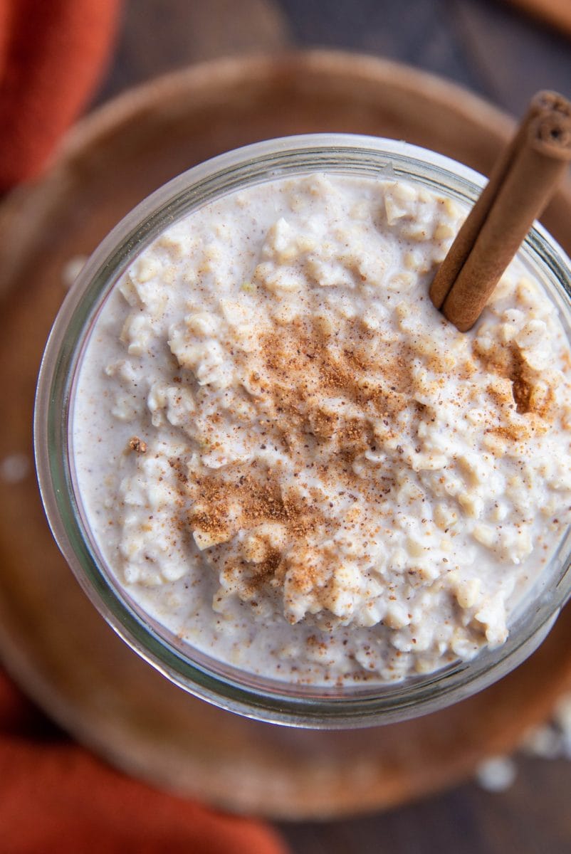 Top down close up image of a jar full of Chai spiced overnight oats with a cinnamon stick inside and a red napkin.