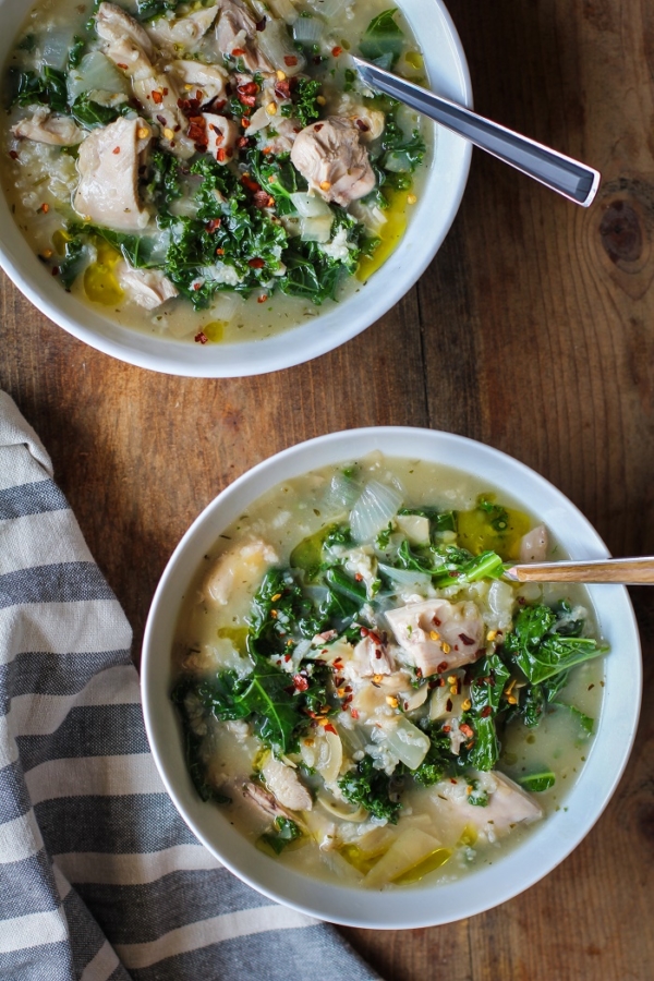 Crock Pot Chicken, Artichoke, and Kale Soup in two bowls with wood inlay spoons, ready to serve.