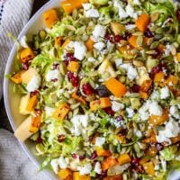 Top down image of big bowl of Shaved Brussel Sprout Salad with roasted butternut squash, pumpkin seeds, feta cheese, and pomegranate seeds on top.