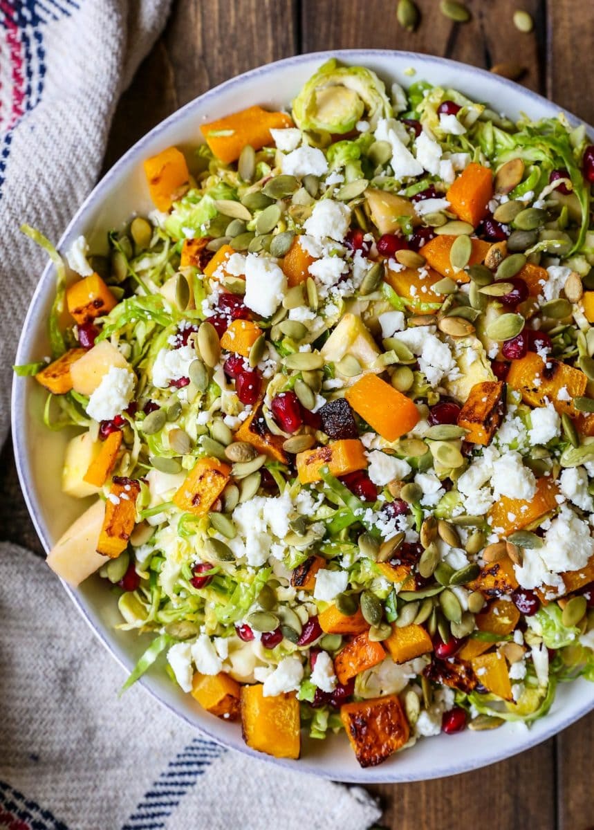 Top down image of big bowl of Shaved Brussel Sprout Salad with roasted butternut squash, pumpkin seeds, feta cheese, and pomegranate seeds on top.