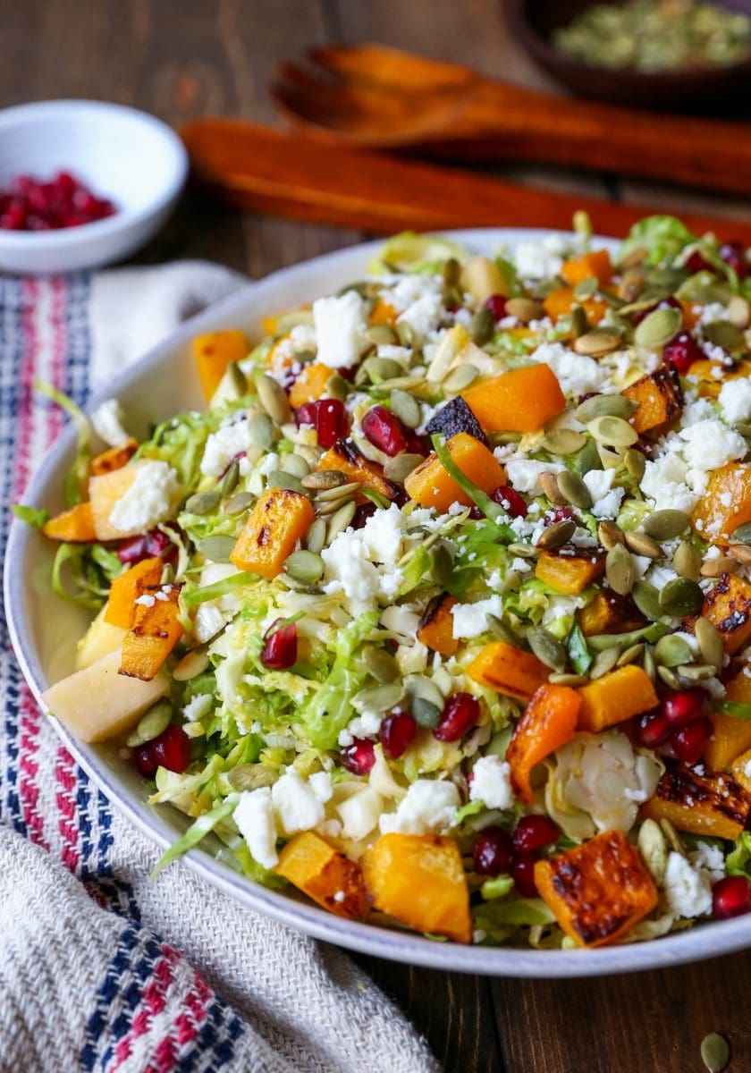 Angled close up shot of Shaved Brussel Sprout Salad with Roasted Butternut Squash, Pomegranate Seeds, Pumpkin Seeds, Feta, and Citrusy Maple Cinnamon Dressing with a napkin to the side