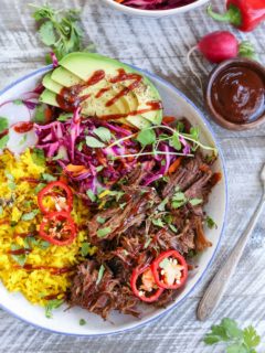 Top down photo of a blue-rimmed bowl with shredded beef, yellow rice, avocado, and slaw inside for the most delicious burrito bowl.