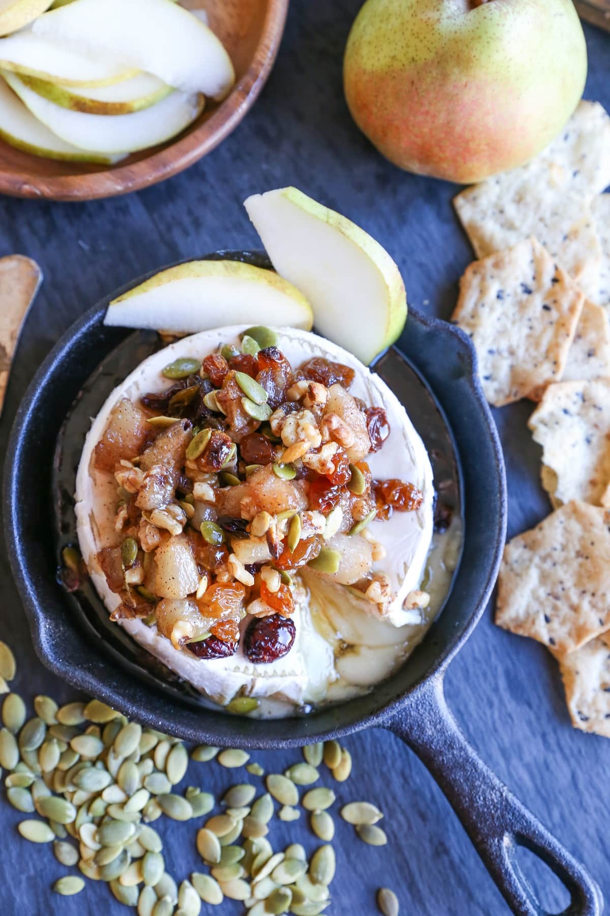 Maple-Spiced Pear Baked Brie with Walnuts, Pumpkin Seeds, and Golden Raisins served with sliced pear and gluten-free crackers. A lovely fall-inspired appetizer!