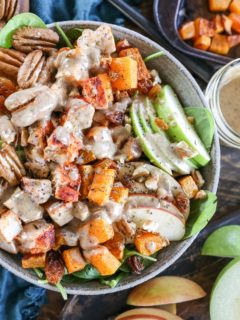 Top down close up image of a rustic bowl full of spinach salad with various ingredients like chicken, apples, pecans, and more.