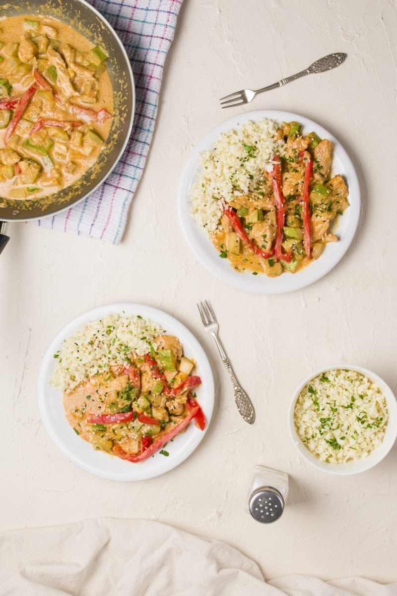 Table of two plates of red curry with cauliflower rice and a skillet with red curry chicken.