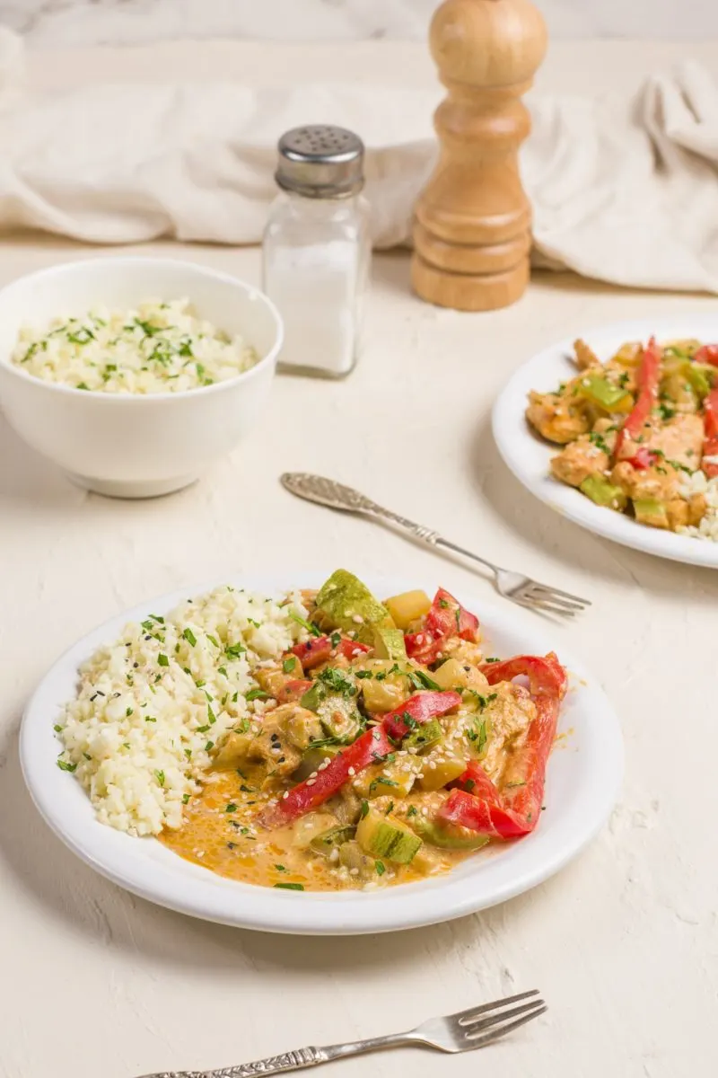 Two bowls of Thai red curry with chicken and vegetables, served with cauliflower rice.