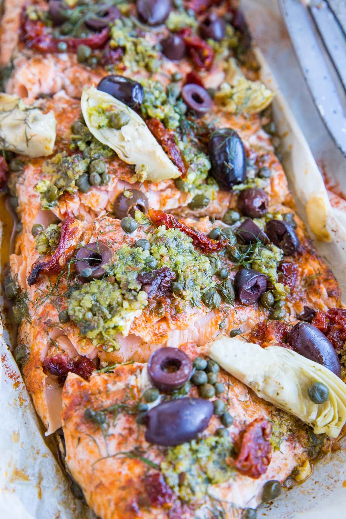 Mediterranean Salmon in Parchment Paper with sun-dried tomatoes, kalamata olives, dill, capers, and artichoke hearts. This easy dinner recipe is paleo, keto, and packed with flavor!