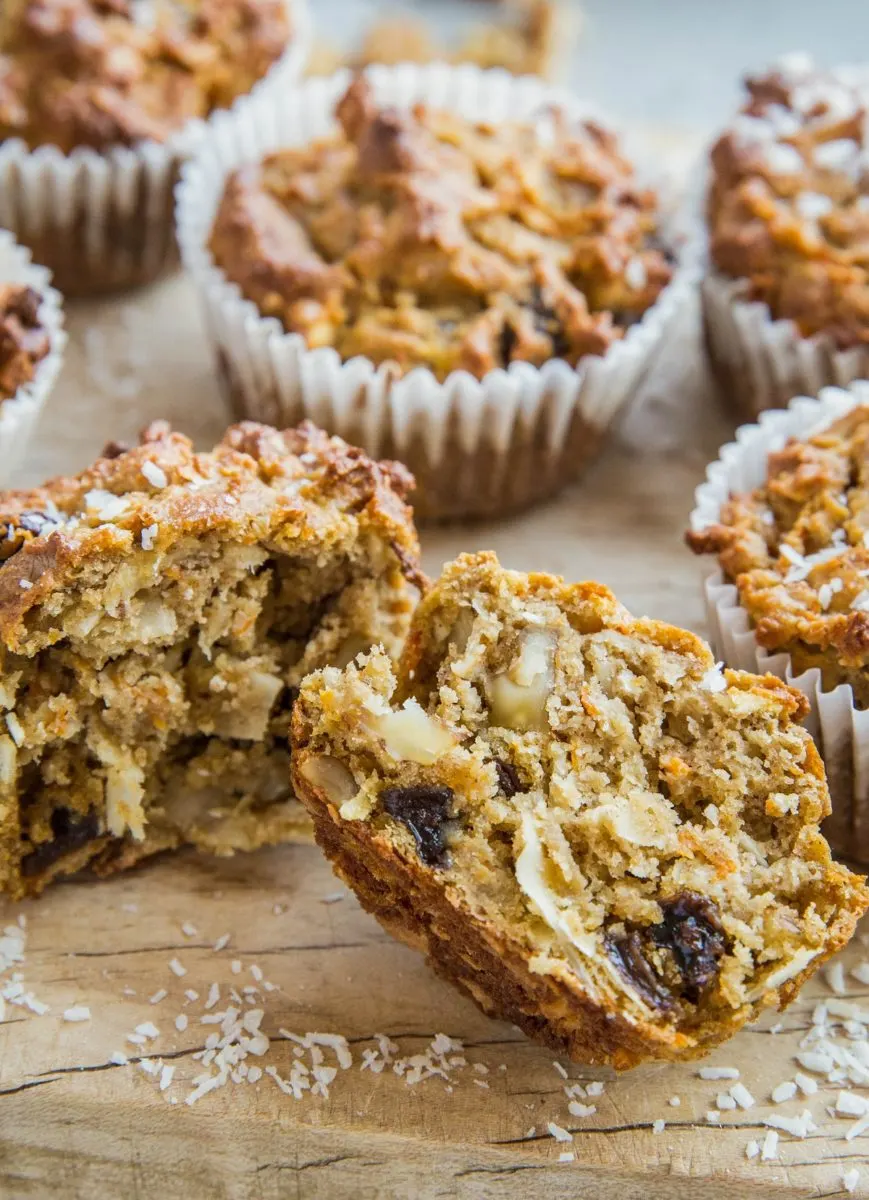 Close up shot of morning glory muffins on a cutting board with one sliced in half so you can see the inside. Coffee in the background.