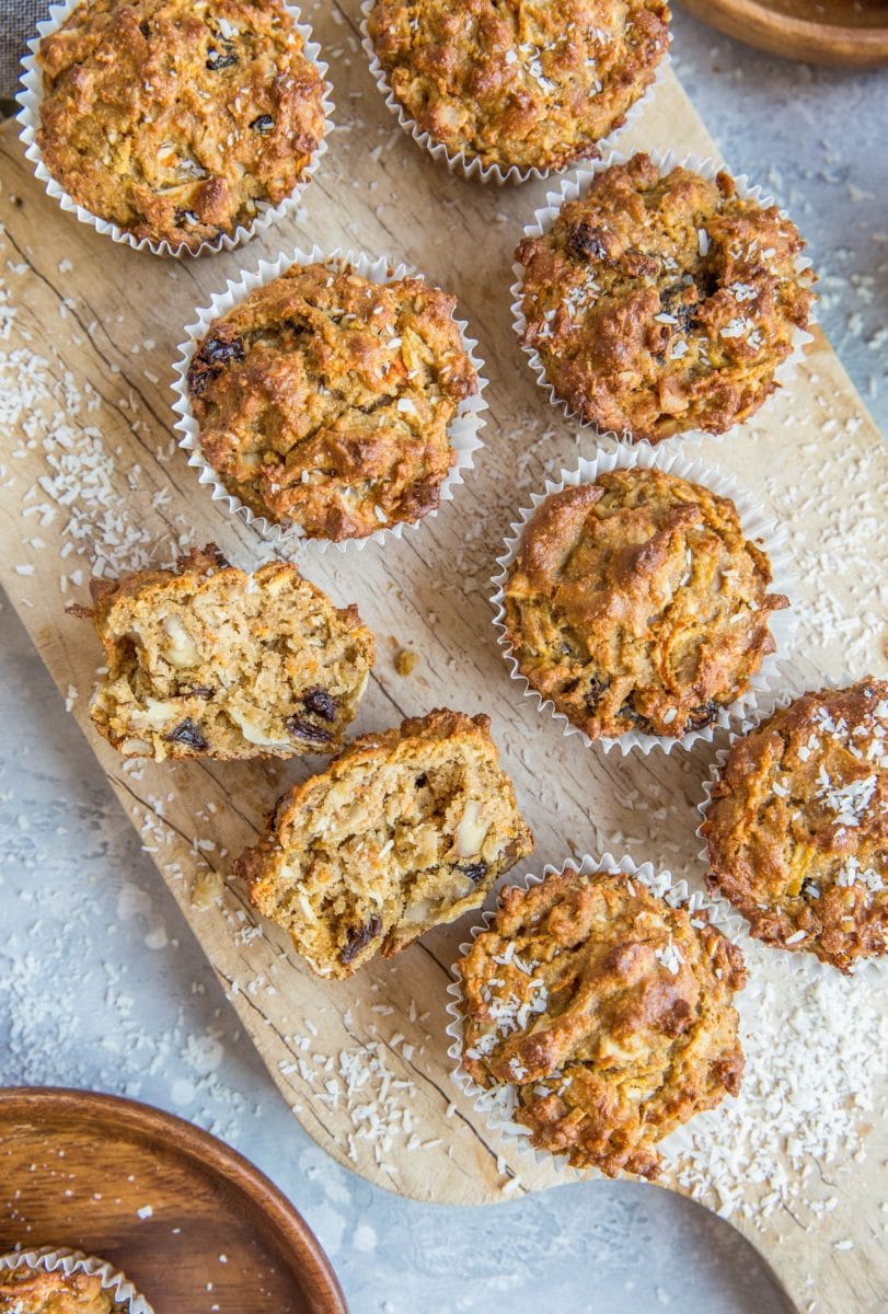 Top down photo of morning glory muffins sitting on a wood cutting board, sprinkled with shredded coconut.