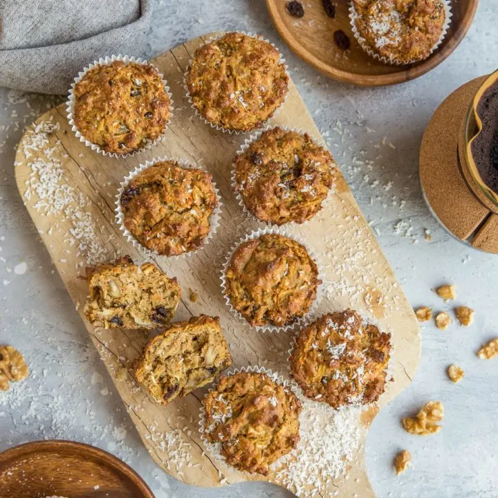 Top down photo of a cutting board of paleo morning glory muffins as well as two wooden plates with muffins on them, ready to eat.