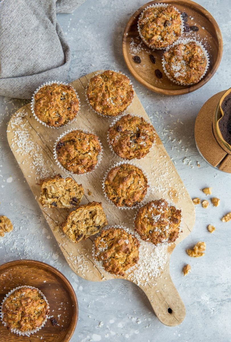 Top down photo of a cutting board of paleo morning glory muffins as well as two wooden plates with muffins on them, ready to eat.