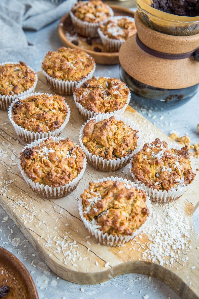 Wooden cutting board with almond flour morning glory muffins sitting on top and a plate of muffins in the background.