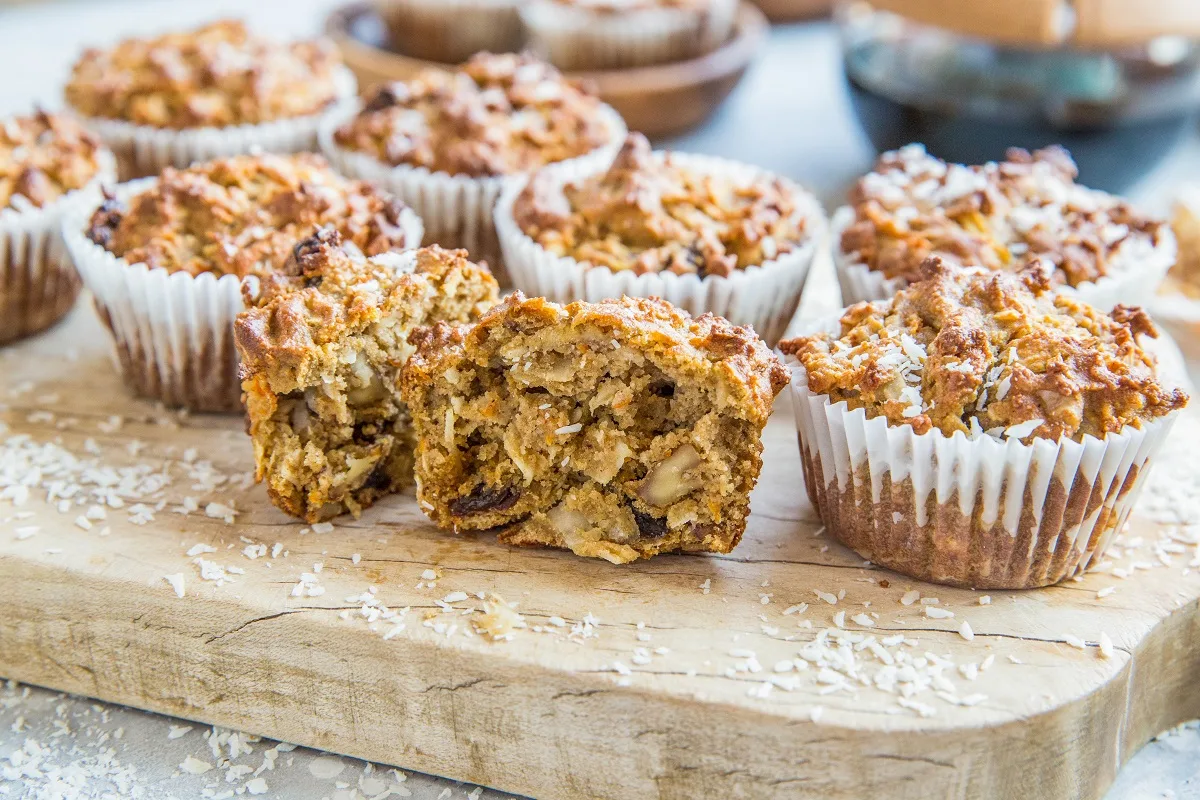 Horizontal image of healthy morning glory muffins sitting on a wooden cutting board with one sliced in half so you can see the inside.