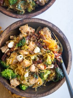 Top down photo of two wooden bowls of chicken spaghetti squash with a golden napkin to the side.