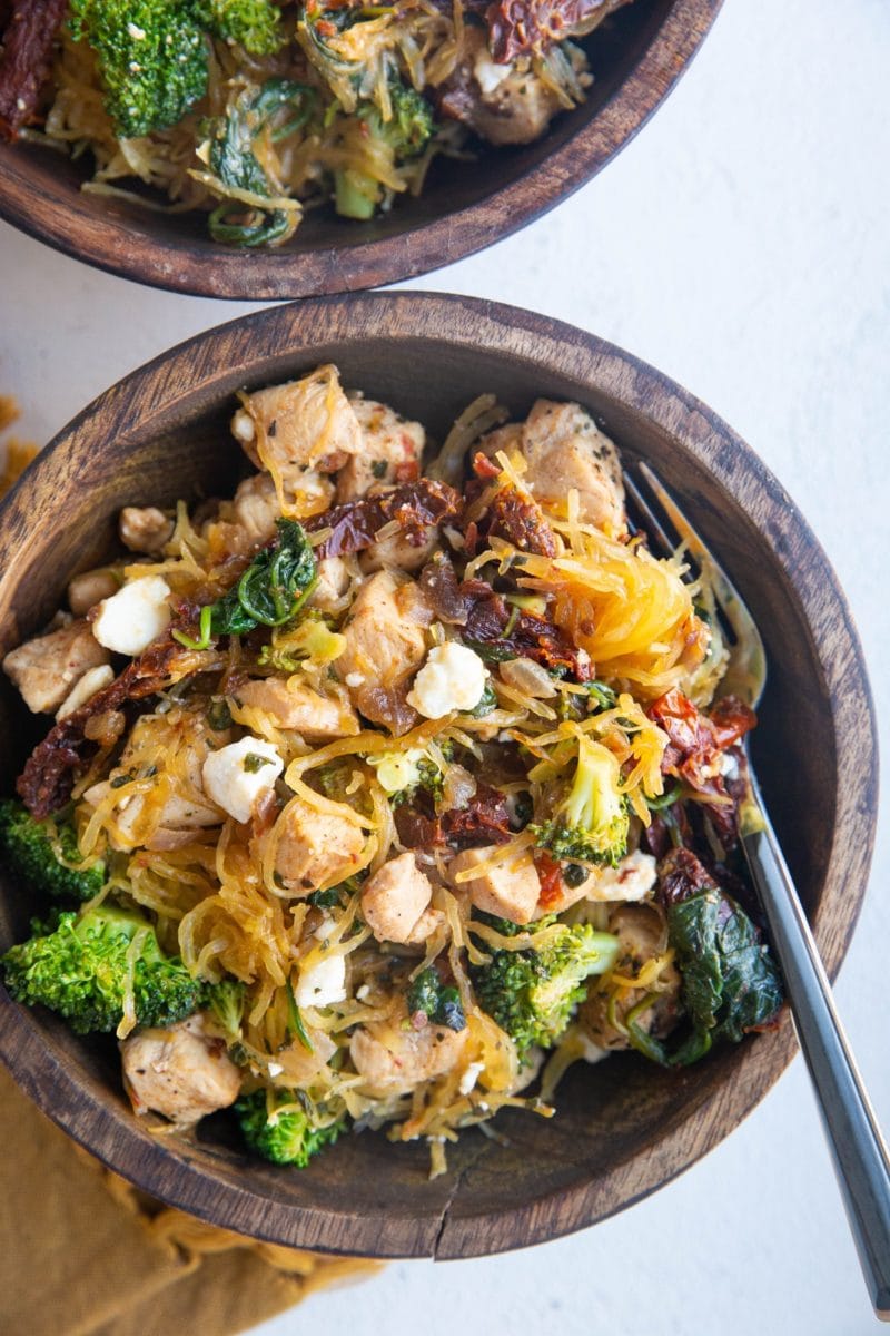 Top down photo of two wooden bowls of chicken spaghetti squash with a golden napkin to the side.