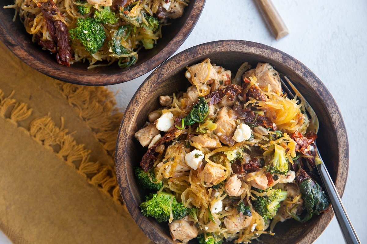 Horizontal photo of two wooden bowls of chicken spaghetti squash with veggies.