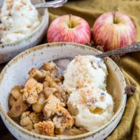 Two bowls of hot apple crisp with scoops of vanilla ice cream