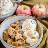 Two bowls of hot apple crisp with scoops of vanilla ice cream