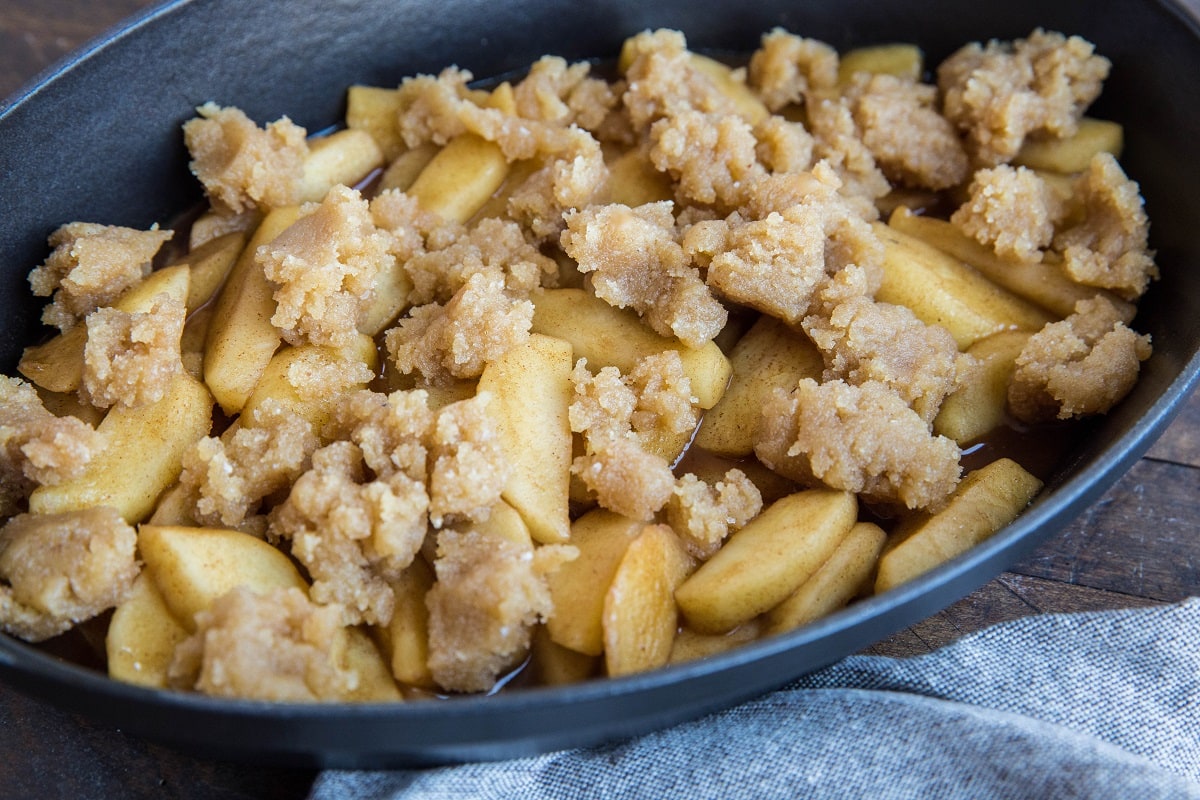 Baking dish with cinnamon spiced apple and almond flour topping, ready to go into the oven to make apple crumble