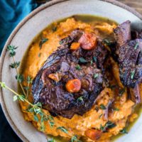 Top down photograph of a ceramic bowl full of mashed sweet potatoes and two short ribs.