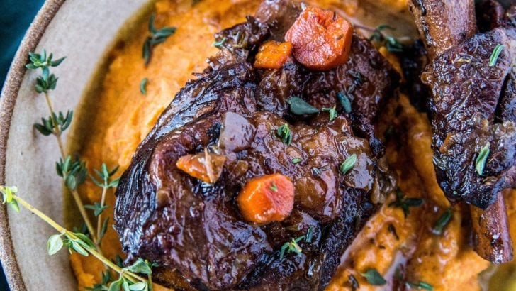 Top down photograph of a ceramic bowl full of mashed sweet potatoes and two short ribs.