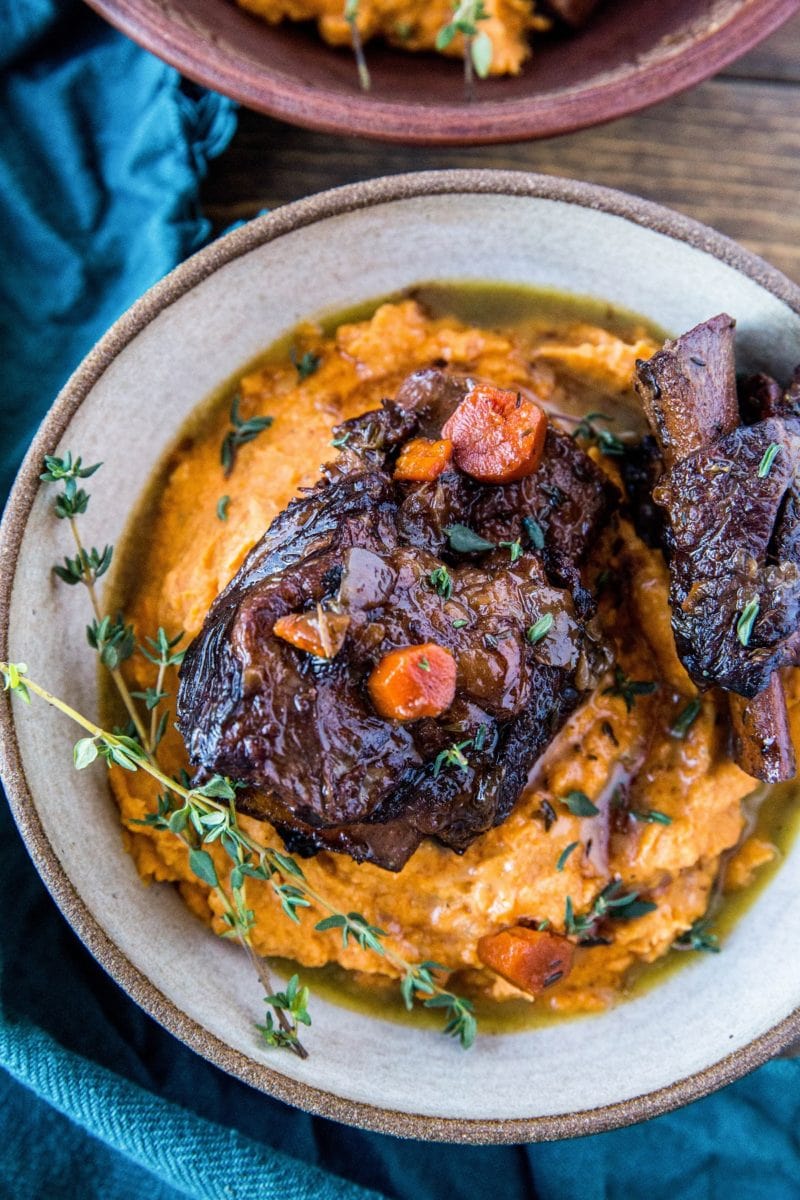 Top down photograph of a ceramic bowl full of mashed sweet potatoes and two short ribs.