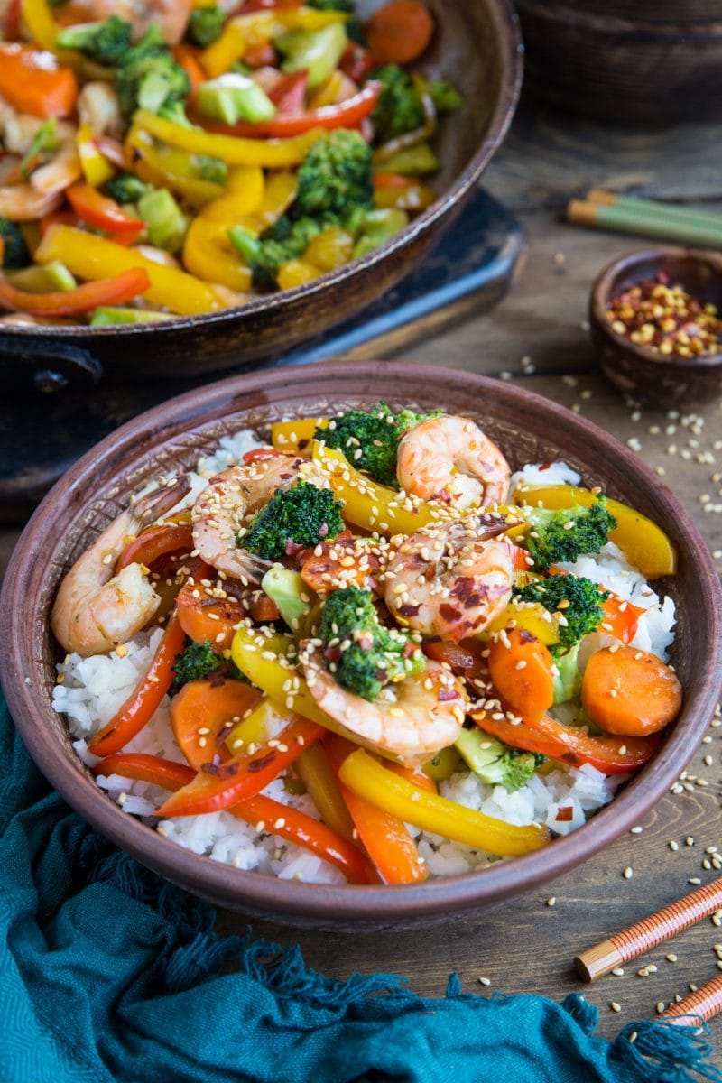 Bowl of shrimp stir fry with a skillet of stir fry in the background.