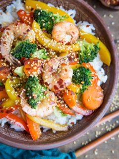 Orange-Ginger Shrimp Stir Fry in a bowl with a napkin and chopsticks to the side.