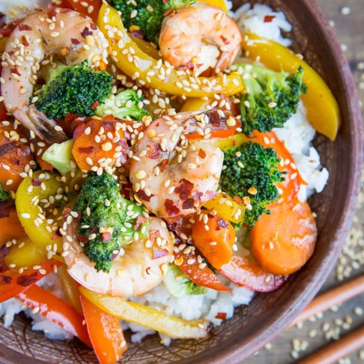 Orange-Ginger Shrimp Stir Fry in a bowl with a napkin and chopsticks to the side.