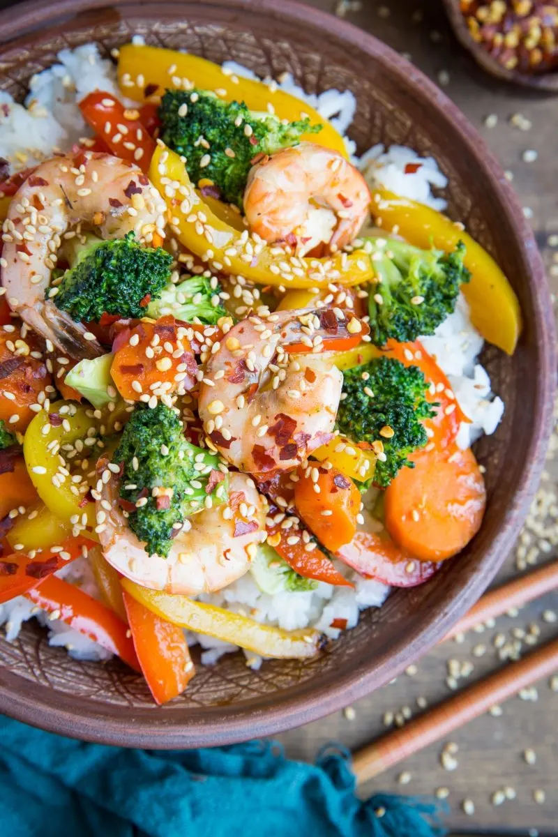 Orange-Ginger Shrimp Stir Fry in a bowl with a napkin and chopsticks to the side.