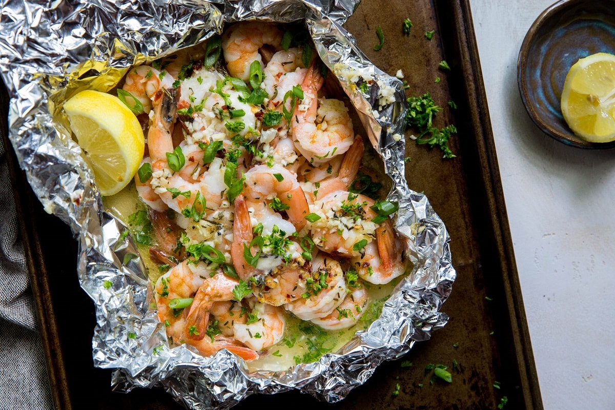 Baking sheet with a foil packet of cooked shrimp with butter and garlic on top. Fresh out of the oven.