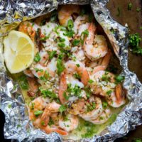 How to Grill Shrimp in Foil Packets. Shrimp foil packet on a baking sheet with fresh herbs sprinkled around.