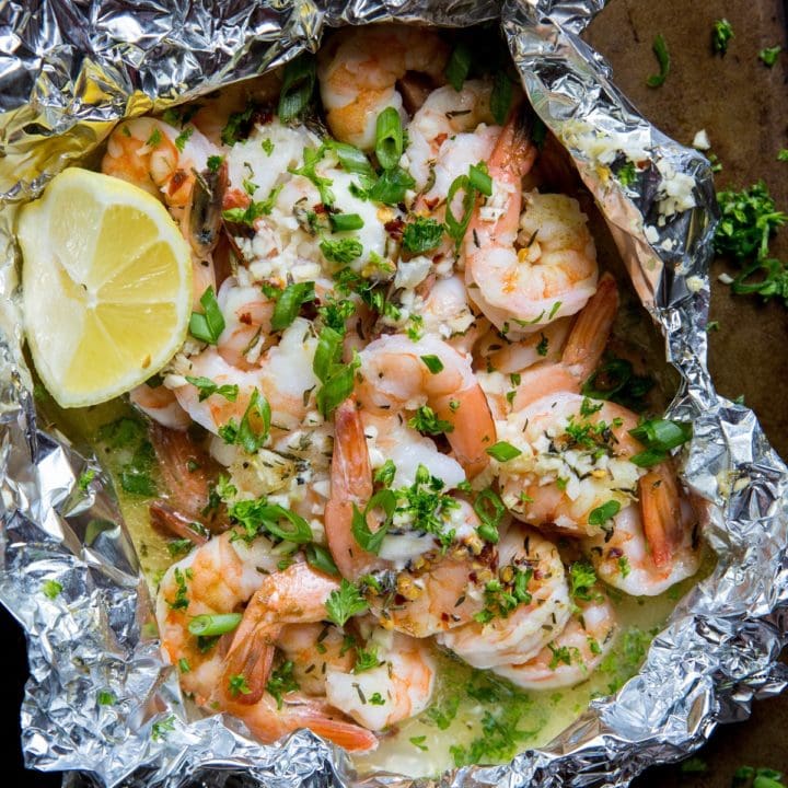 How to Grill Shrimp in Foil Packets. Shrimp foil packet on a baking sheet with fresh herbs sprinkled around.